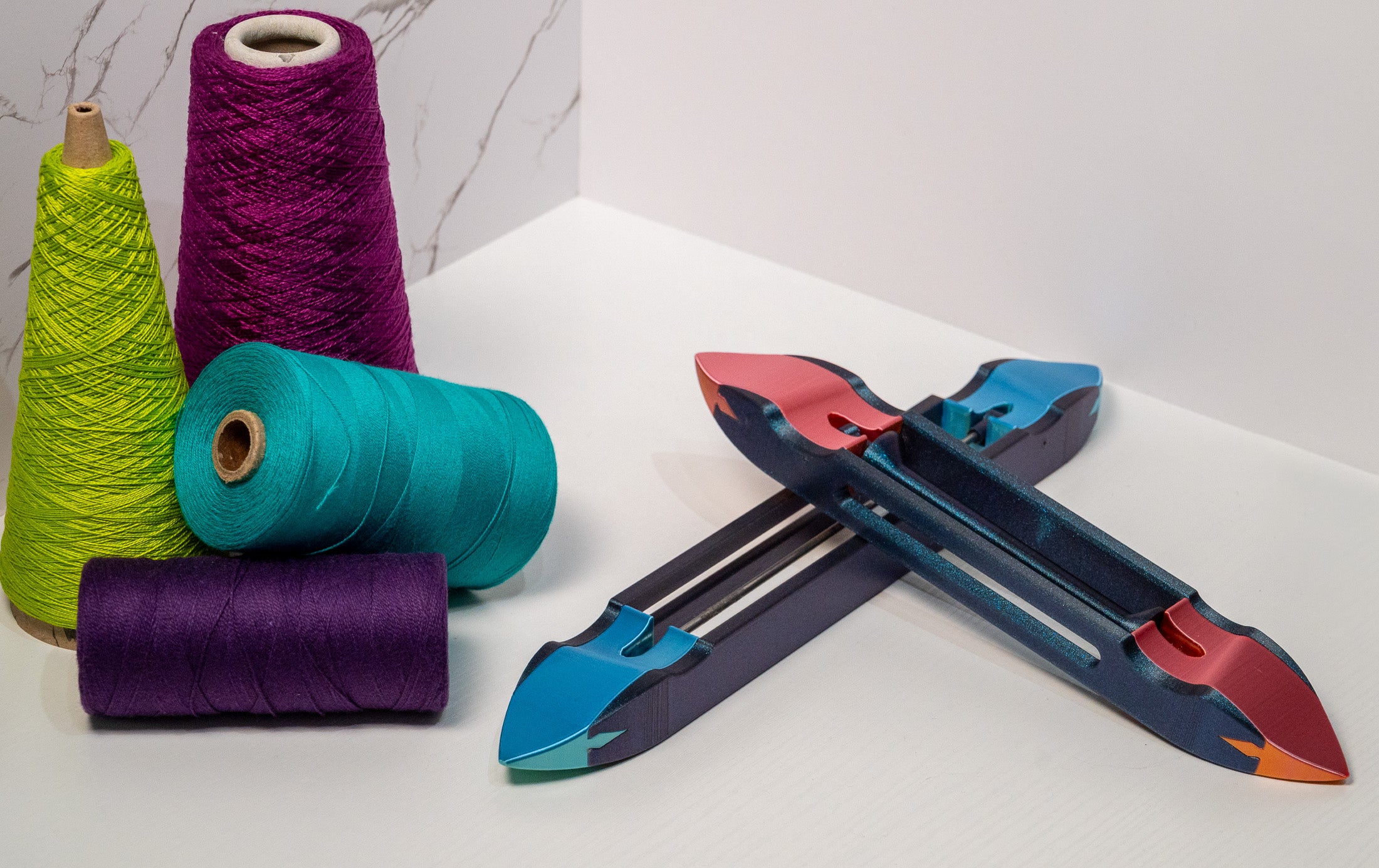 An image of two 3D Printed boat shuttles displayed alongside several cones of yarn